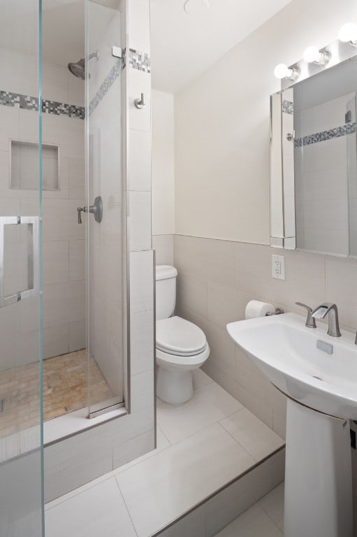 bathroom featuring toilet, a stall shower, tile walls, tile patterned floors, and a sink