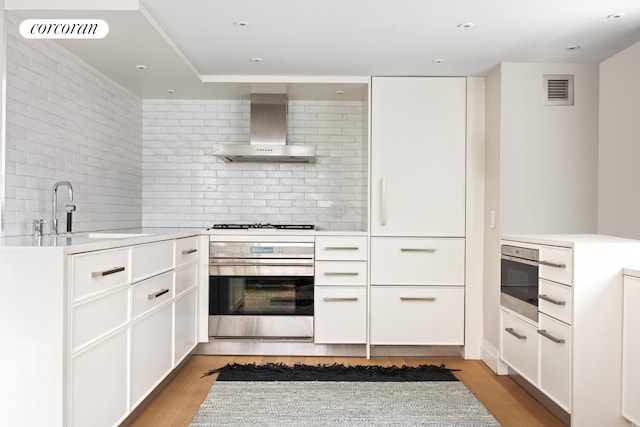 421 Hudson St Unit 214, New York City, NY 10014 - kitchen featuring wall chimney exhaust hood, stainless steel oven, a sink, light countertops, and backsplash