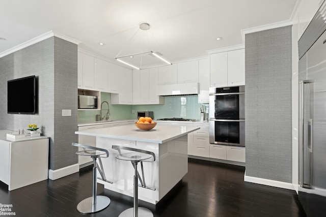 kitchen featuring appliances with stainless steel finishes, under cabinet range hood, dark wood finished floors, a sink, and crown molding