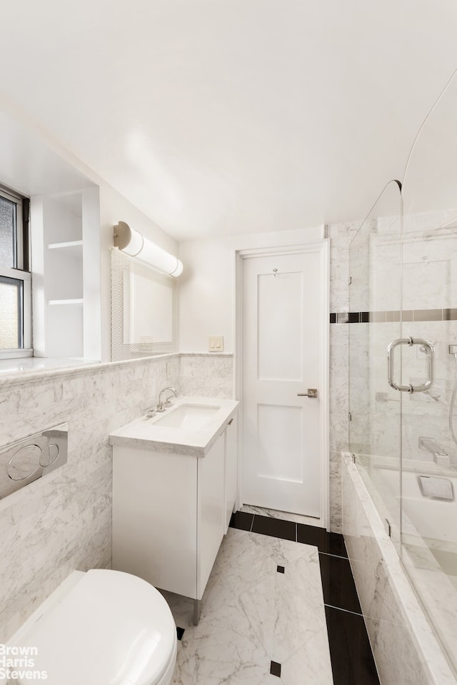 bathroom featuring tile walls, combined bath / shower with glass door, vanity, and toilet