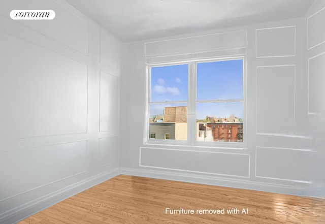 spare room featuring light wood-type flooring, baseboards, and a decorative wall