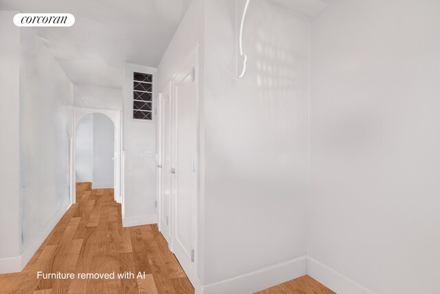 hallway featuring light wood-type flooring, baseboards, and arched walkways