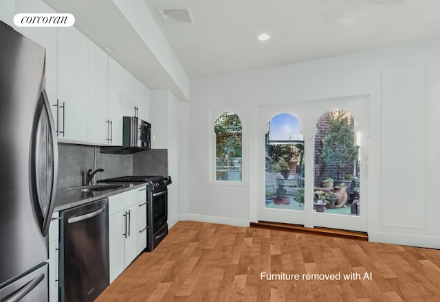 kitchen featuring stainless steel appliances, a sink, decorative backsplash, white cabinets, and light wood-style floors