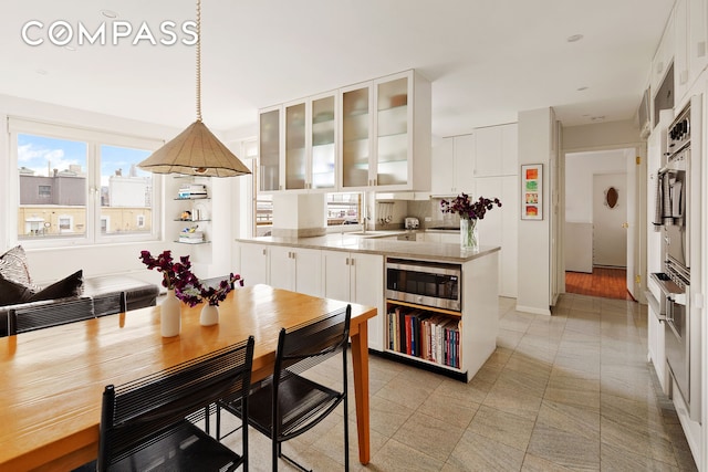 kitchen with a peninsula, stainless steel microwave, white cabinetry, glass insert cabinets, and decorative light fixtures