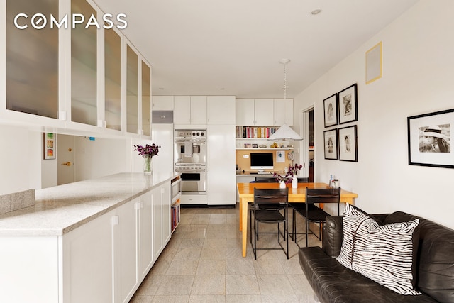 kitchen with white cabinets, stainless steel double oven, a breakfast bar, and glass insert cabinets