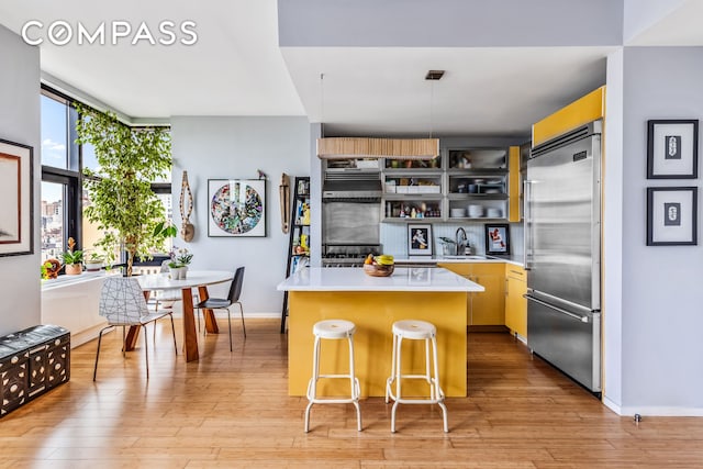 kitchen featuring built in refrigerator, a sink, light countertops, a kitchen island, and light wood finished floors