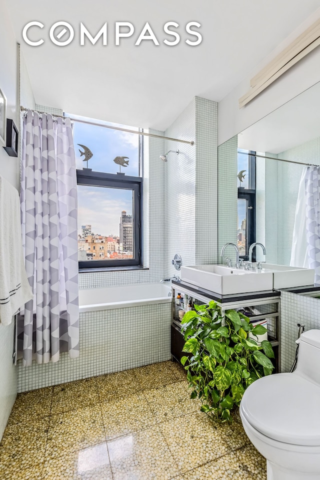 full bathroom with healthy amount of natural light, toilet, vanity, and tiled shower / bath combo