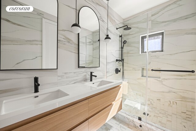full bath with double vanity, tile walls, a marble finish shower, and a sink