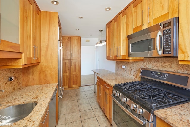 kitchen with appliances with stainless steel finishes, a sink, light stone counters, and backsplash