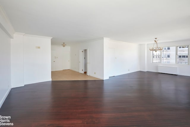 unfurnished living room featuring crown molding, an inviting chandelier, wood finished floors, and baseboards
