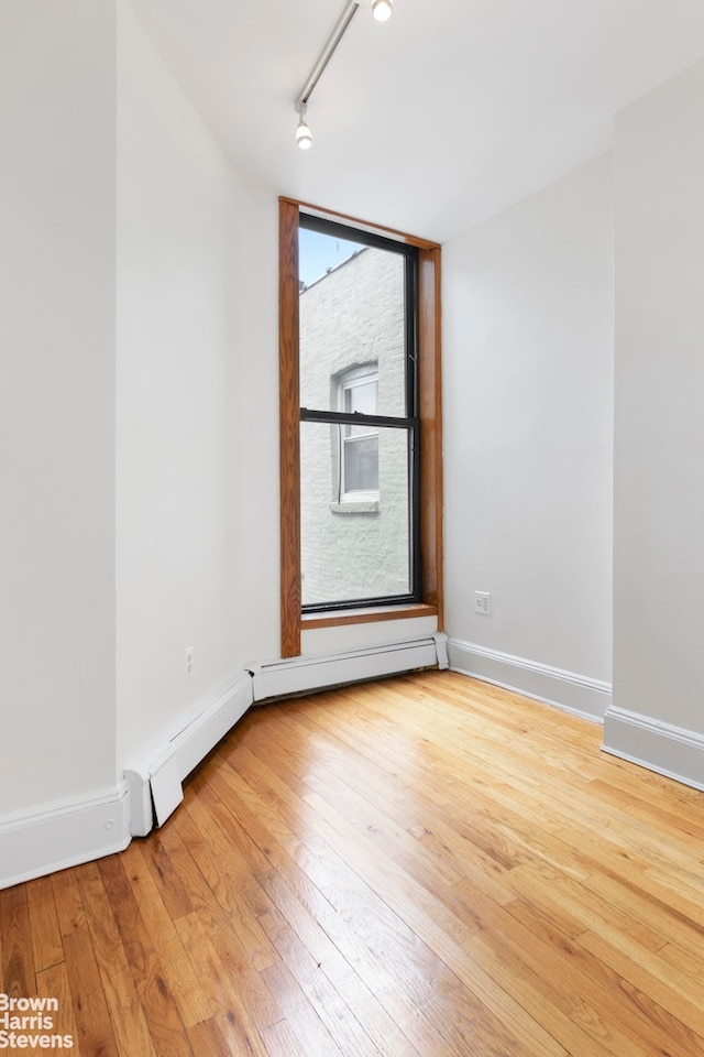 unfurnished room with track lighting, light wood-style flooring, baseboards, and baseboard heating