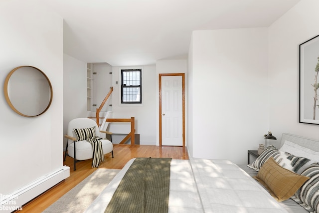 bedroom featuring a baseboard heating unit, baseboards, and wood finished floors