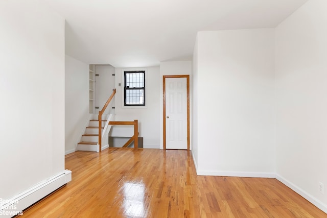 spare room featuring a baseboard radiator, baseboards, and light wood finished floors