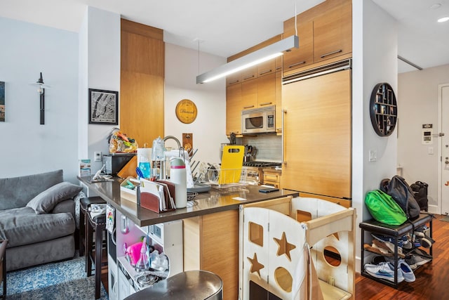 kitchen featuring stainless steel microwave, wood finished floors, tasteful backsplash, dark countertops, and a kitchen bar