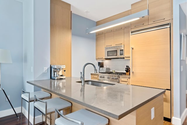 kitchen featuring high end appliances, a sink, a breakfast bar, tasteful backsplash, and a peninsula