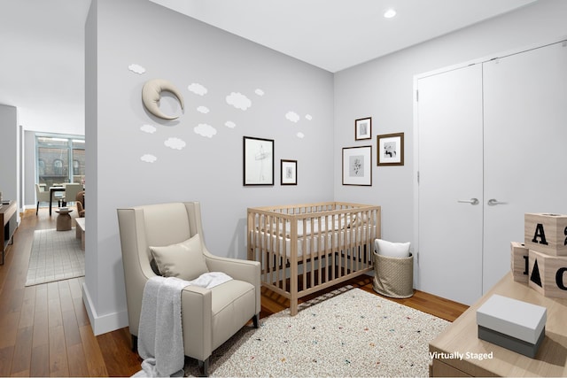 bedroom featuring wood finished floors, a nursery area, a closet, recessed lighting, and baseboards