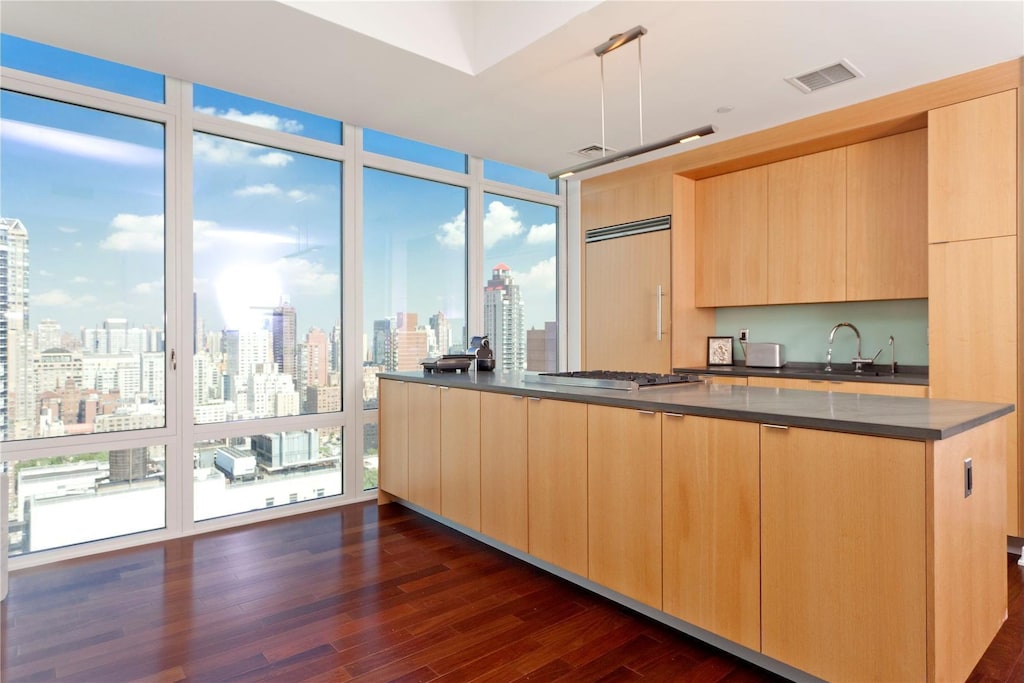 kitchen with a sink, modern cabinets, light brown cabinets, visible vents, and dark countertops