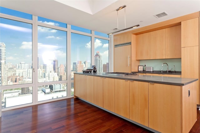 kitchen with a sink, modern cabinets, light brown cabinets, visible vents, and dark countertops