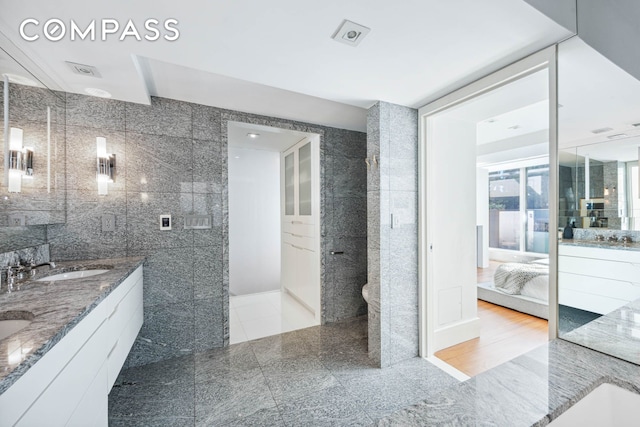 bathroom featuring connected bathroom, tile walls, double vanity, and granite floors