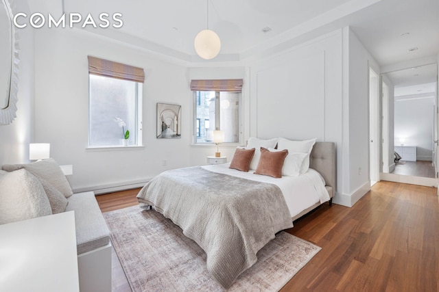 bedroom with wood finished floors, a baseboard heating unit, a tray ceiling, and baseboards