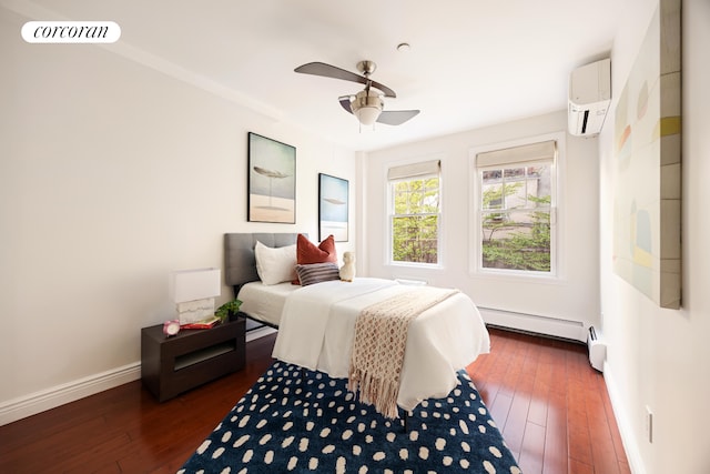 bedroom with a baseboard heating unit, ceiling fan, baseboards, an AC wall unit, and hardwood / wood-style floors