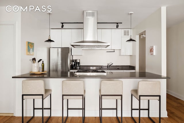 222 W 14th St Unit 3N, New York City, NY 10011 - kitchen with island range hood, stainless steel appliances, a sink, dark countertops, and white cabinets
