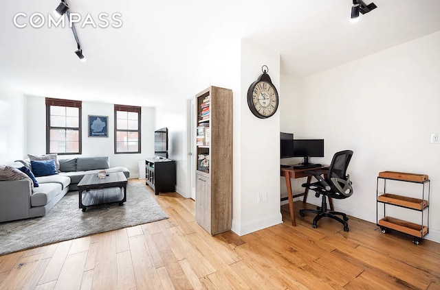 living area with light wood-style flooring, rail lighting, a desk, and baseboards
