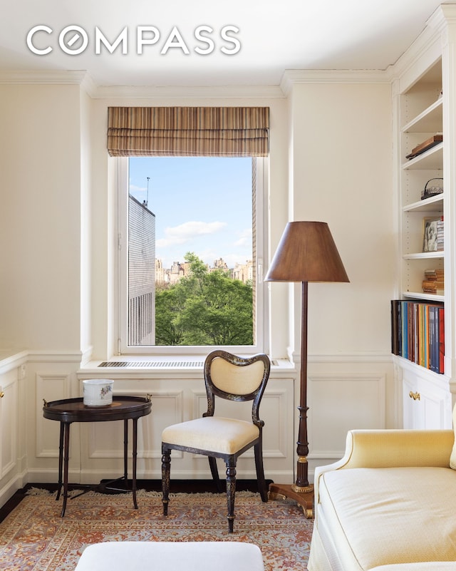 sitting room featuring crown molding, a wainscoted wall, and a decorative wall