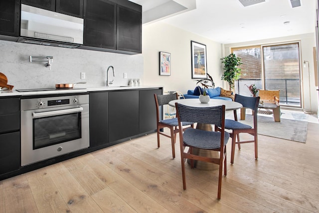 kitchen with oven, dark cabinetry, light countertops, and light wood finished floors