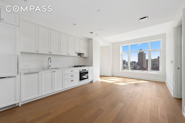 kitchen with appliances with stainless steel finishes, a sink, decorative backsplash, light wood-style floors, and baseboards