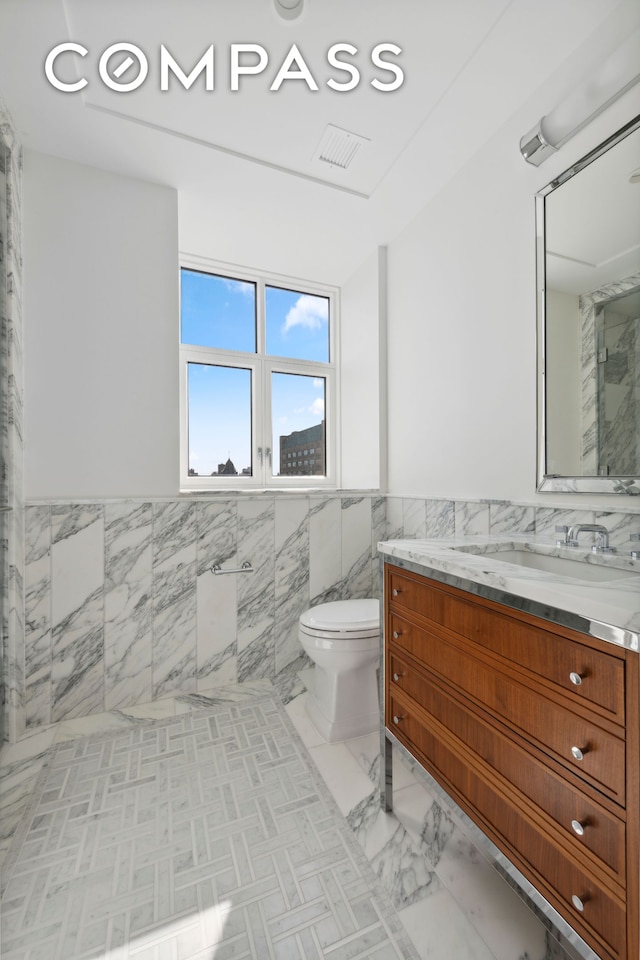 bathroom with tile walls, toilet, vanity, a walk in shower, and wainscoting