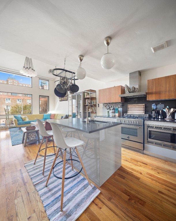 41 Wolcott Street House, New York City, NY 11231 - kitchen featuring wall chimney exhaust hood, appliances with stainless steel finishes, a sink, a kitchen bar, and brown cabinetry
