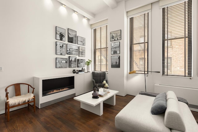 living area featuring dark wood-type flooring, beamed ceiling, and a glass covered fireplace