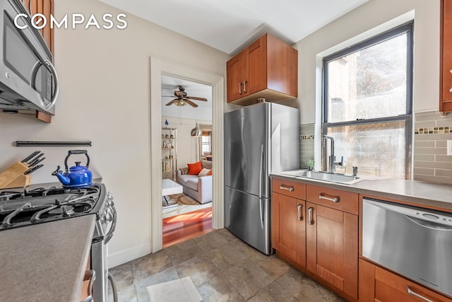 411 W 44th St Unit 13, New York City, NY 10036 - kitchen featuring stainless steel appliances, a sink, backsplash, a ceiling fan, and brown cabinetry