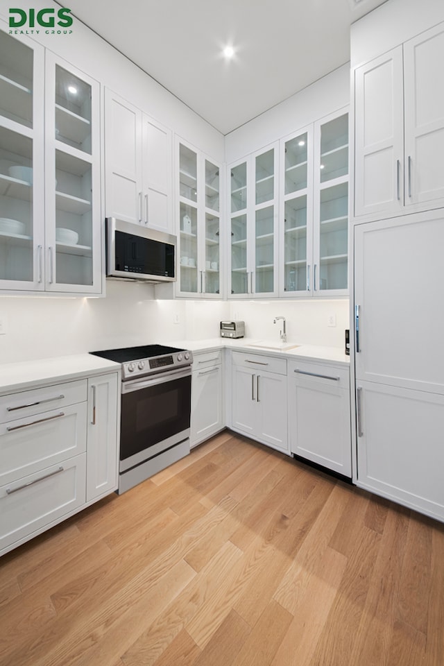 kitchen with electric range, stainless steel microwave, light countertops, light wood finished floors, and glass insert cabinets
