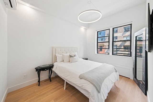 bedroom with light wood-style floors, a wall mounted AC, and baseboards