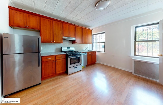 kitchen featuring stainless steel appliances, light wood-style flooring, brown cabinetry, light countertops, and under cabinet range hood