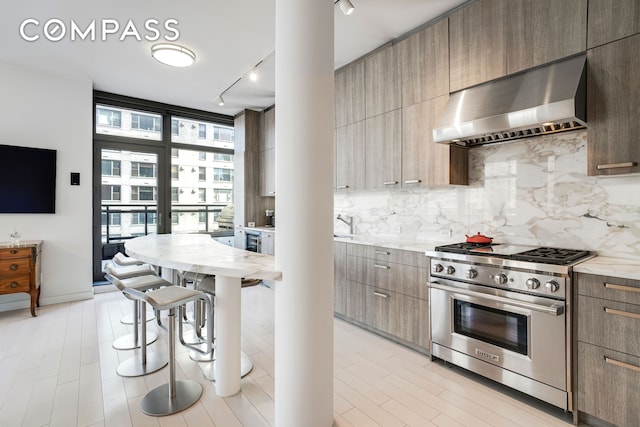 450 E 83rd St Unit 6B, New York City, NY 10028 - kitchen with wall chimney exhaust hood, luxury range, rail lighting, modern cabinets, and tasteful backsplash