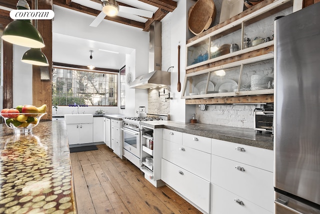 kitchen featuring wall chimney range hood, white cabinetry, a sink, appliances with stainless steel finishes, and dark countertops