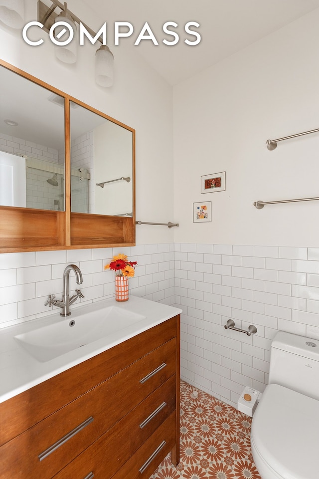 bathroom featuring vanity, toilet, tile walls, tile patterned floors, and a wainscoted wall