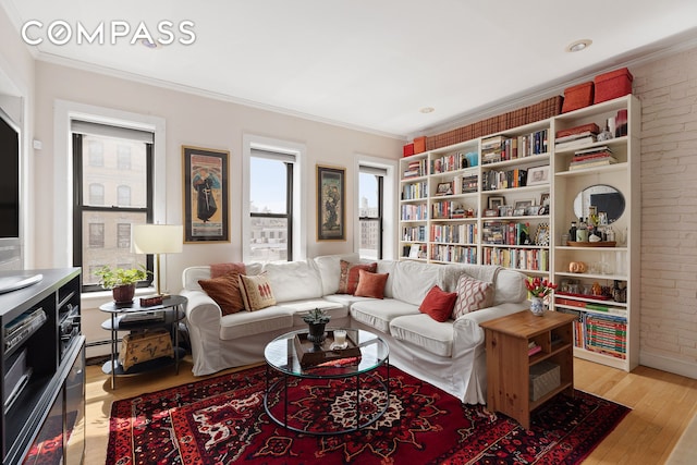 living room featuring light wood-type flooring, ornamental molding, brick wall, and baseboard heating