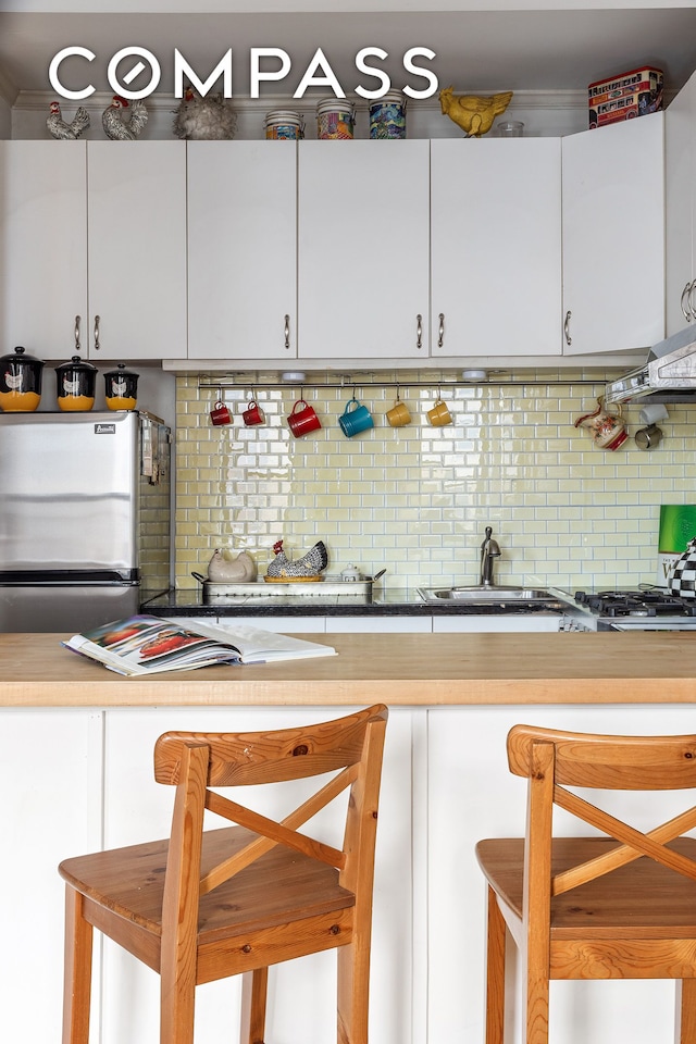 kitchen with backsplash, a sink, light countertops, freestanding refrigerator, and white cabinetry