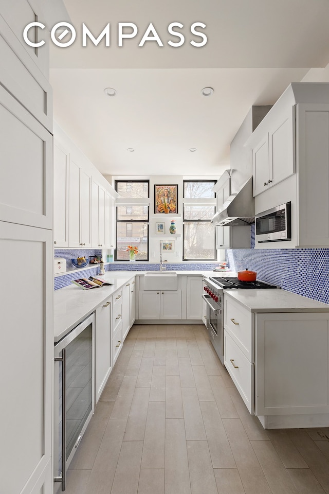 kitchen featuring open shelves, beverage cooler, wall chimney range hood, tasteful backsplash, and appliances with stainless steel finishes