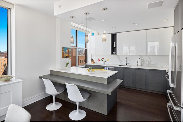 kitchen featuring stainless steel refrigerator, modern cabinets, dark wood-style floors, a breakfast bar area, and a sink