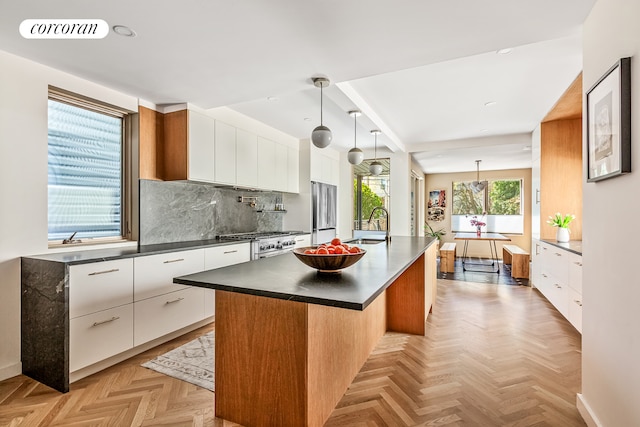 kitchen featuring modern cabinets, dark countertops, appliances with stainless steel finishes, a sink, and a center island with sink