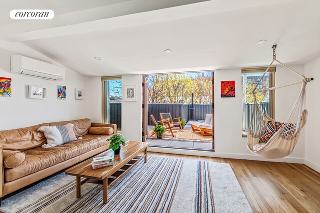 living area with an AC wall unit, wood finished floors, baseboards, recessed lighting, and vaulted ceiling