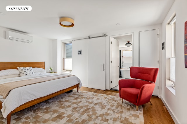 bedroom featuring a wall mounted air conditioner, light wood-style floors, baseboards, and a barn door