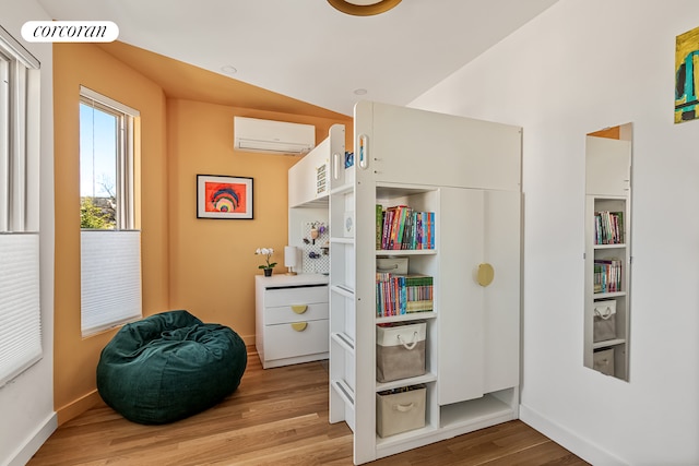 bedroom with a wall unit AC, light wood finished floors, baseboards, and an office area