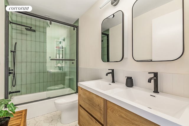 bathroom with combined bath / shower with glass door, toilet, double vanity, a wainscoted wall, and tile patterned floors