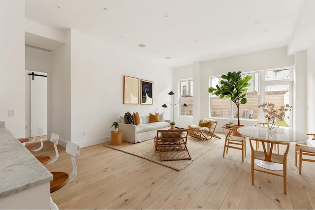 living area with baseboards, a barn door, and light wood-style floors